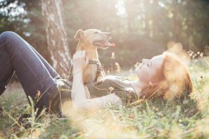 young woman Lying On Back in grass and playing with her small Mixed-breed dog